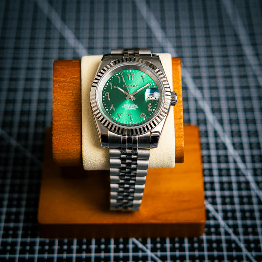 une montre seiko mod arabic dial green muni d'un jubilee bracelet sur un fond cadrillé noir