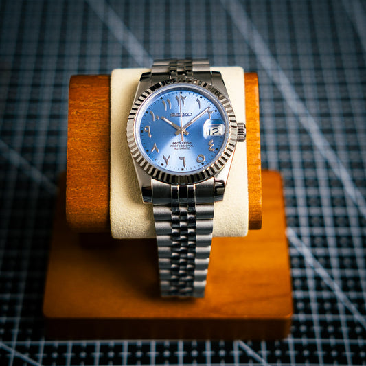 une montre seiko mod arabic dial blue ice munie d'un jubilee bracelet sur une planche à découper noire